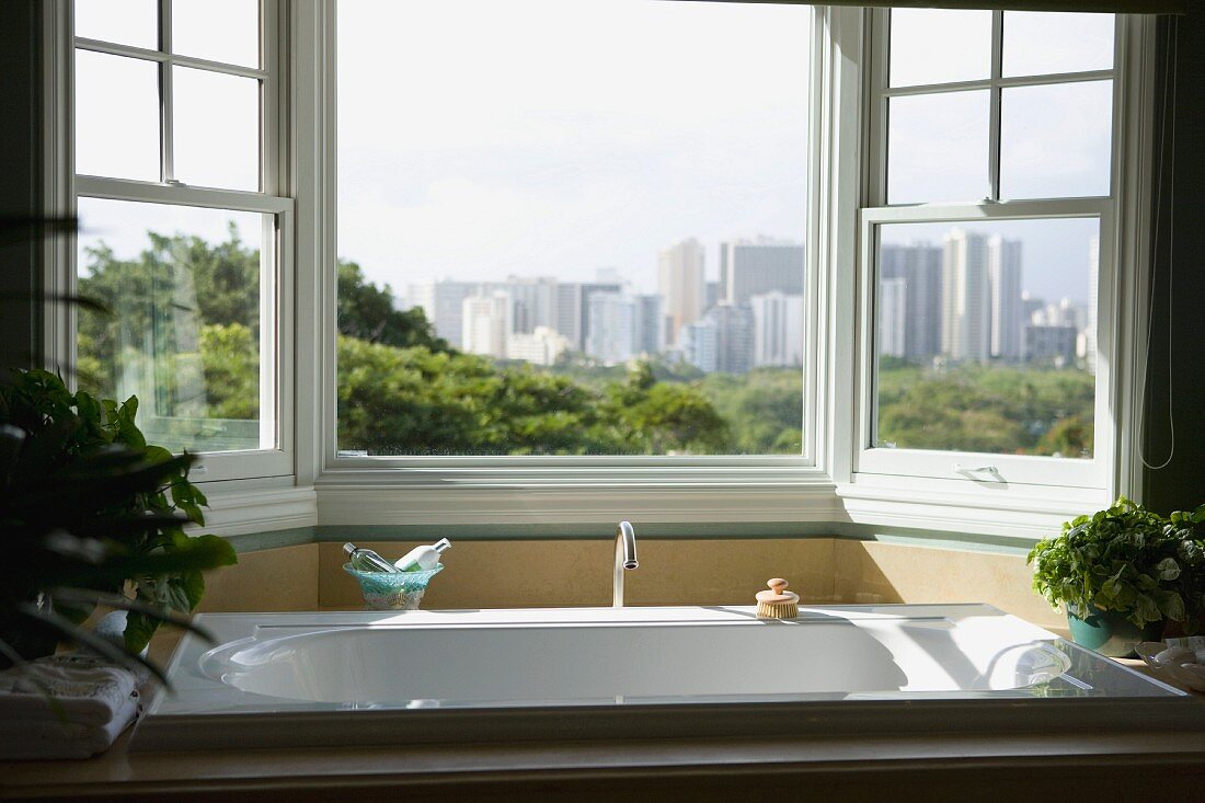 Freistehende, moderne Badewanne vor geöffnetem Erkerfenster mit Blick auf Hochhauskulisse