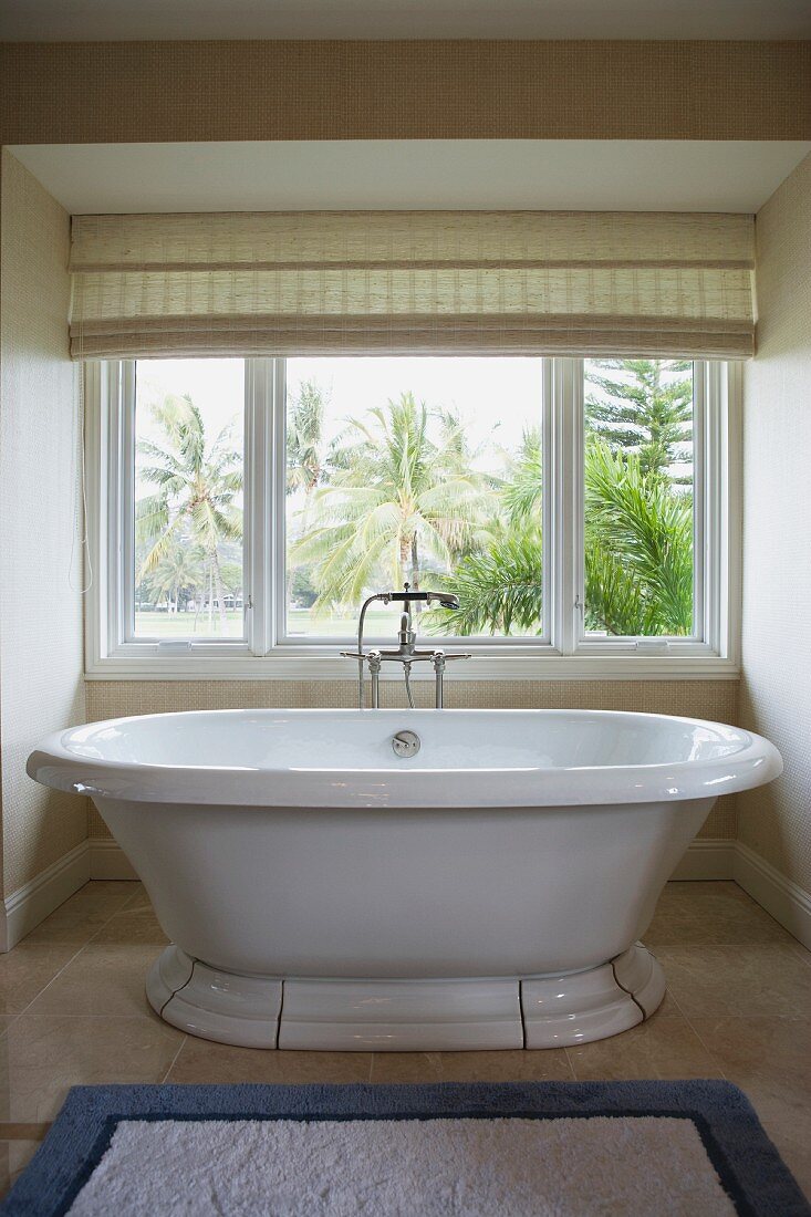 Schmales Bad mit freistehender Wanne vor dem Fenster und Ausblick auf Palmen