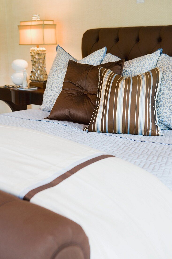 Braun gepolstertes Doppelbett mit hellblau / braun gemusterten Kissen und Decken