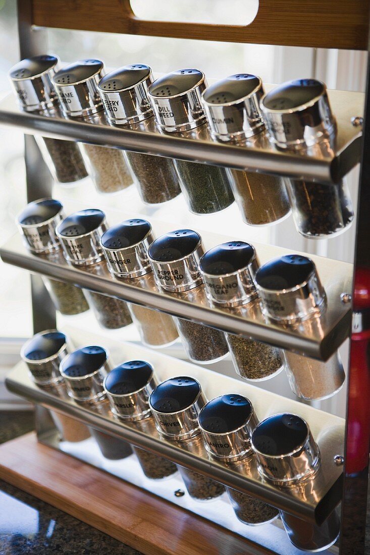 Dreireihiger, moderner Gewürzständer mit beschrifteten Metalldeckeln auf Glasflaschen