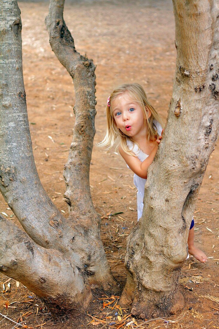 Blondes Mädchen spielt am Baum