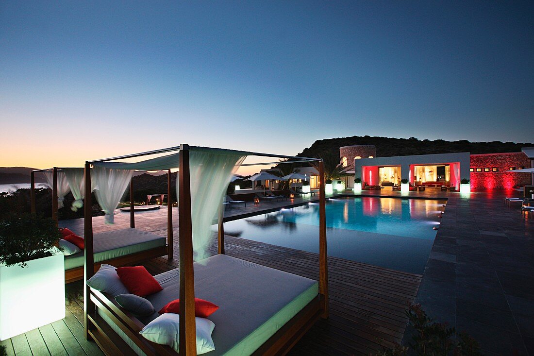Outdoor Himmelbett vor Pool und zeitgenössisches Wohnhaus mit Lichtinszenierung in Nachtstimmung