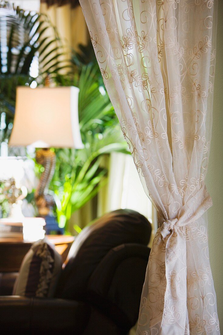 Drapierte Voilegardine im Wohnzimmer mit unscharfem Sessel und Stehlampe im Hintergrund