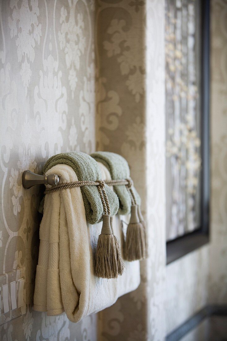 Gefaltete und mit Quastenkordeln zusammengebundene Handtücher vor eleganter Tapete