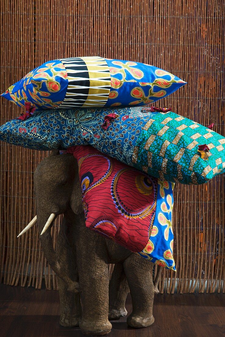 Stack of colourful cushions on back of wooden elephant figure in front of bamboo curtain