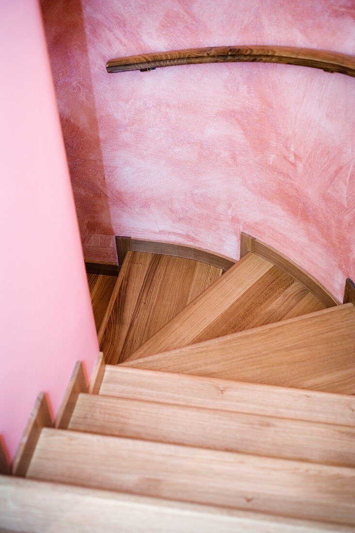 Wooden stair treads and handrail on curved, pink wall