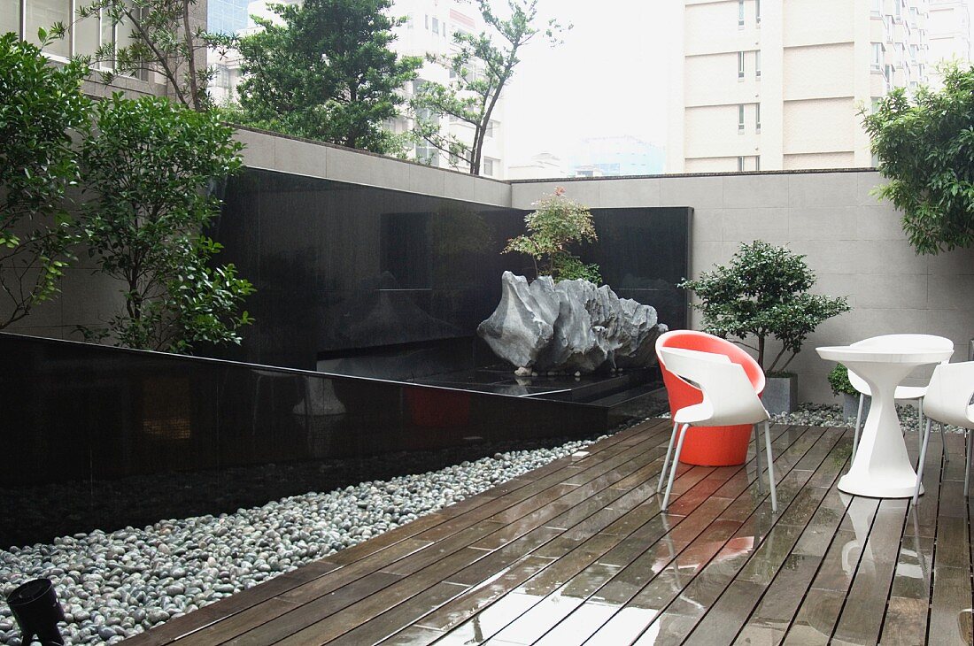 Designer Outdoormöbel auf regennasser Holzterrasse im Innenhof zeitgenössischer Architektur