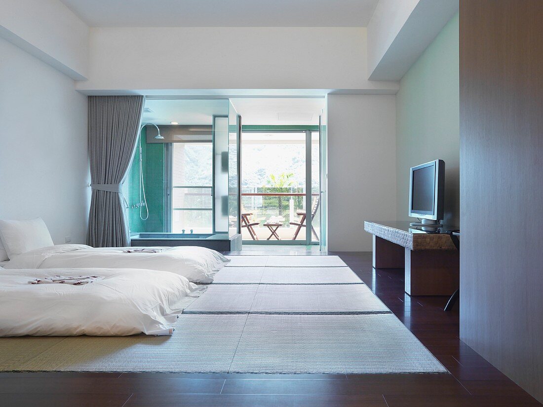 Futon Einzelbetten auf Bodenmatten und Duschbereich an Fensterfront im minimalistischen Schlafzimmer