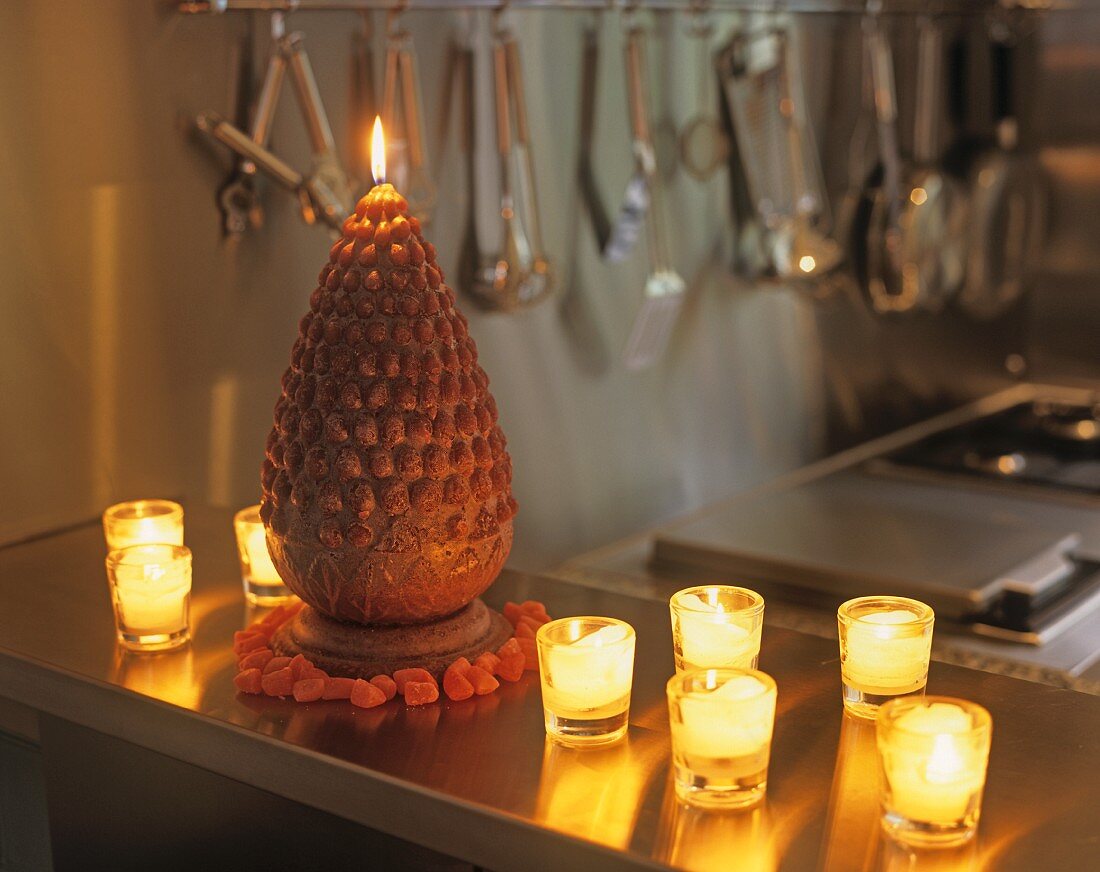 Windlichtgläser mit brennenden Kerzen neben kegelförmiger Kerze auf Ablage in der Küche