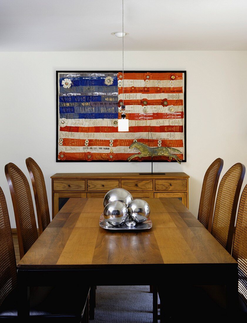 Esstisch aus dunklem Holz und Stühle mit Geflecht an Rückenlehne vor gemalter amerikanischer Flagge an Wand