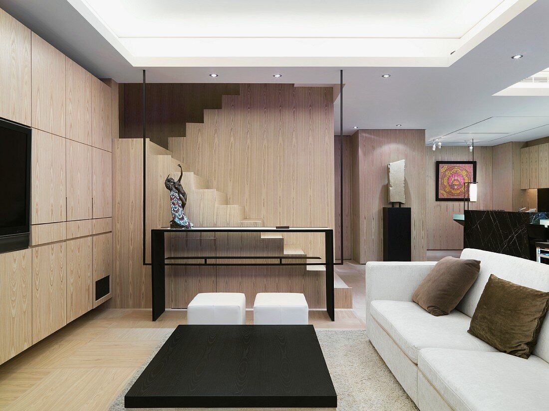 Modernes, klares Wohnzimmer mit glatter Schrankfront und einem Treppenaufgang; davor eine Glastrennwand mit Metallrahmen