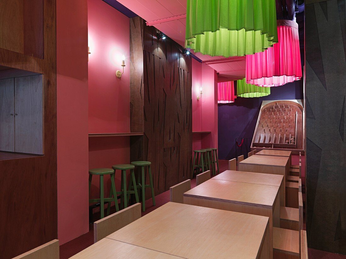 Inneraum eines Cafés mit einfachen, quadratischen Holztischen und bunten Stofflampen
