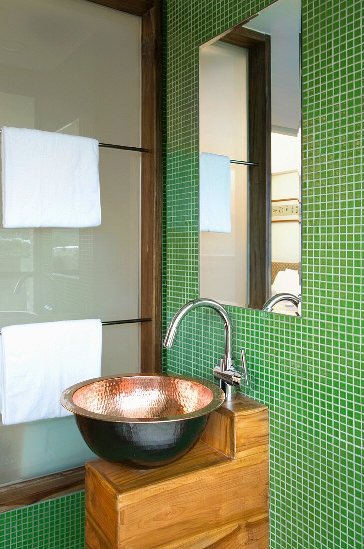 Badezimmer mit grünen Mosaikfliesen und einer Kupferwaschschüssel auf einem einfachen Waschtisch aus Holz