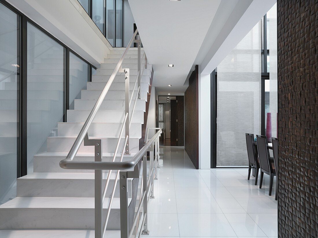 Weisser Treppenaufgang mit Metallhandlauf im offenen Wohnraum; an der Seite die Esszimmerstühle