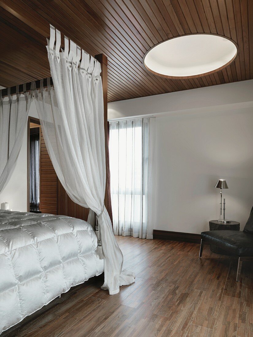 Modernes Schlafzimmer mit Holzboden und Holzdecke; ein rundes Deckenfenster sorgt für mehr Helligkeit im Raum