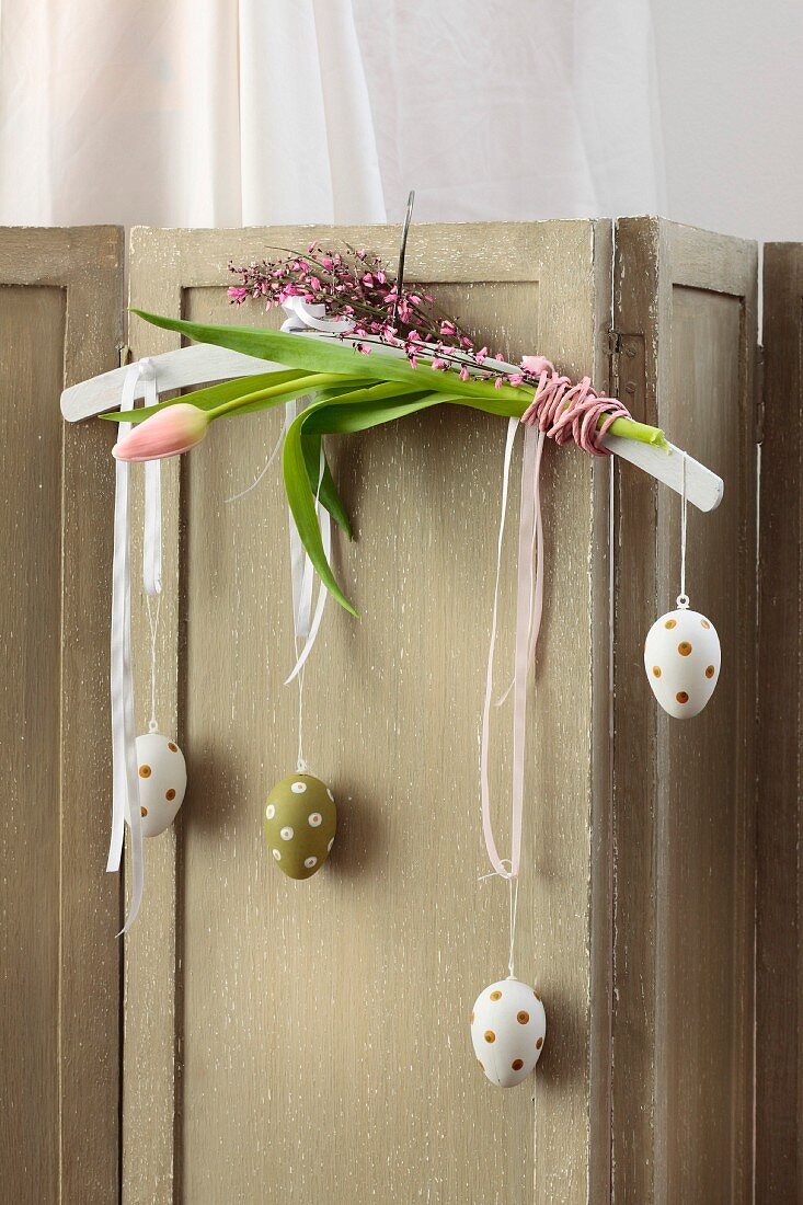White clothes hanger decorated with pink flowers and polka-dot Easter eggs hooked over vintage screen