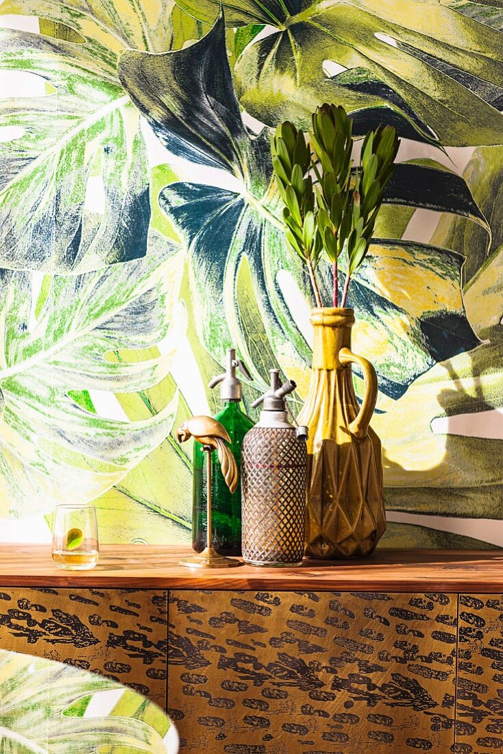 Vase and soda bottles on a Leo chest of drawers in front of jungle wallpaper