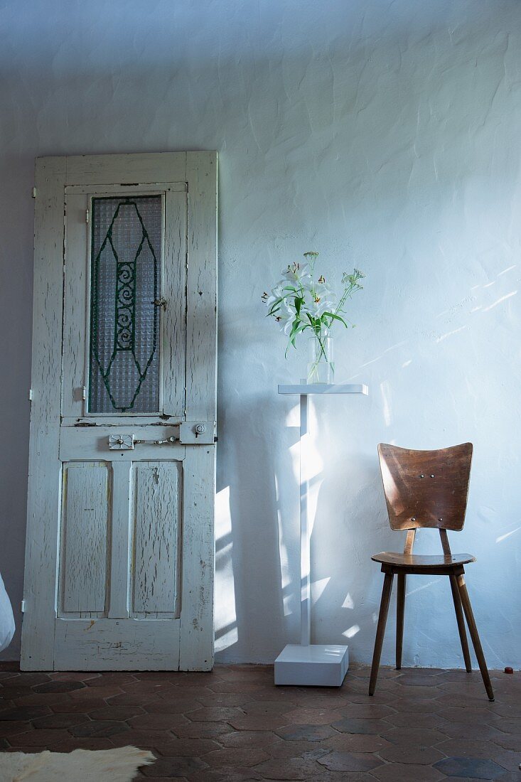 An Wand gelehnte Vintagetür, Blumenständer und Retro-Holzstuhl