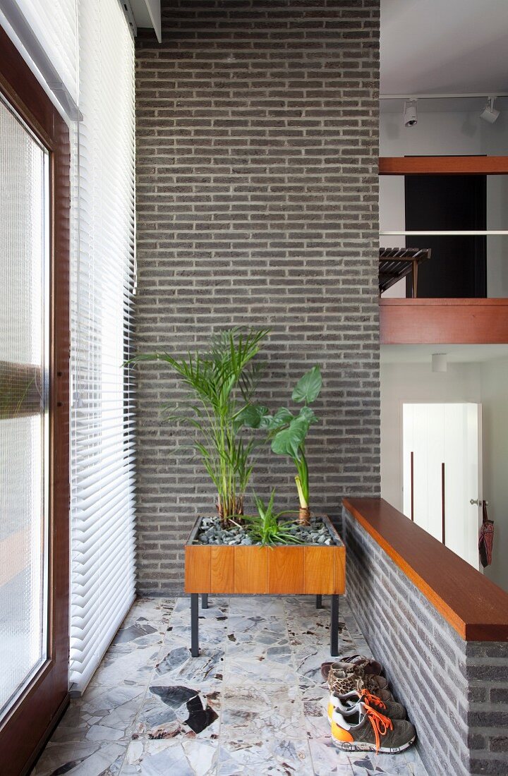 Wooden indoor planter box on legs against brick wall in 60s-style hallway