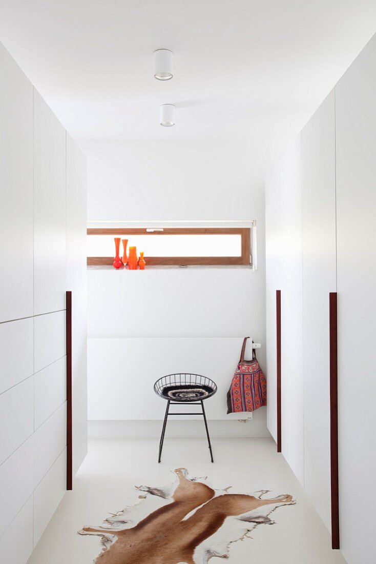 Animal-skin rug on white floor between white fitted wardrobes and delicate black metal stool in minimalist dressing room