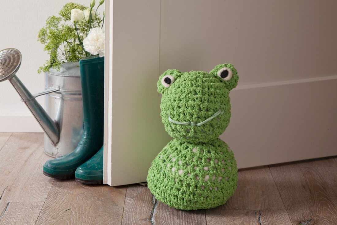 Crocheted frog doorstop on wooden floor