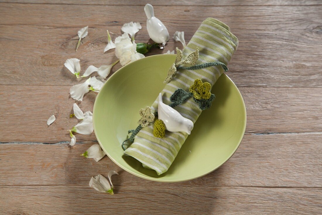 Springlike arrangement of crocheted flowering tendril wrapped around linen napkin on green plate on table