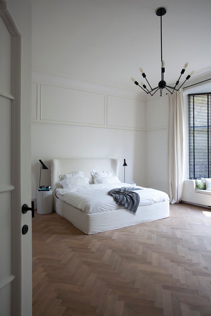 Double bed with tall, white headboard in minimalist bedroom with herringbone parquet floor seen through open door