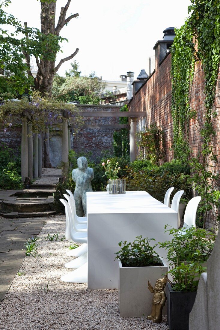 Weißer Tisch und Klassiker Schalenstühle in traditionellem Innenhof vor begrünter Ziegelmauer