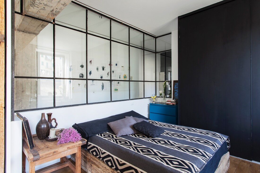 Doppelbett mit folkloristischem Plaid, an verglaster Wand, seitlich schwarzer Einbauschrank