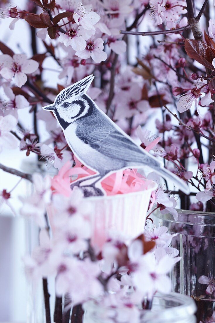 A paper bird with a paper muffin case nest in a sprig of blossom