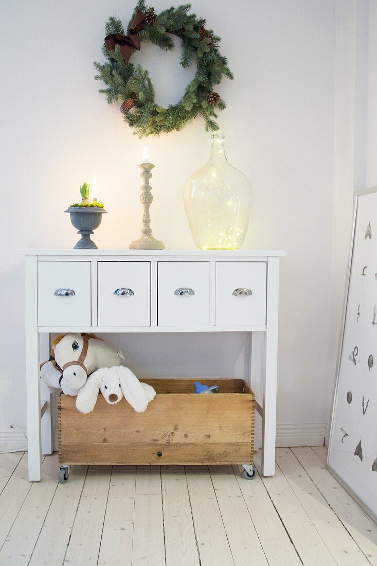 Wreath above white sideboard with wooden crate of toys