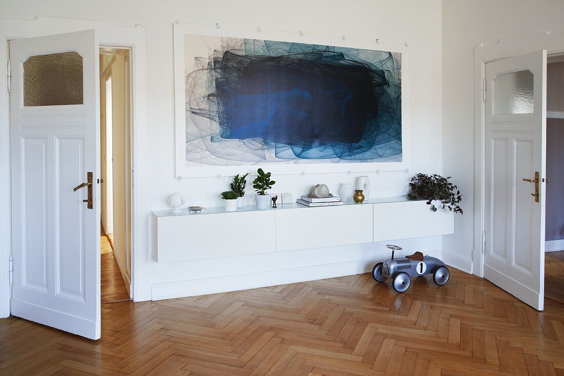 Blaues Gemälde über Lowboard an weisser Wand in Wohnzimmer mit Fischgrätparkett