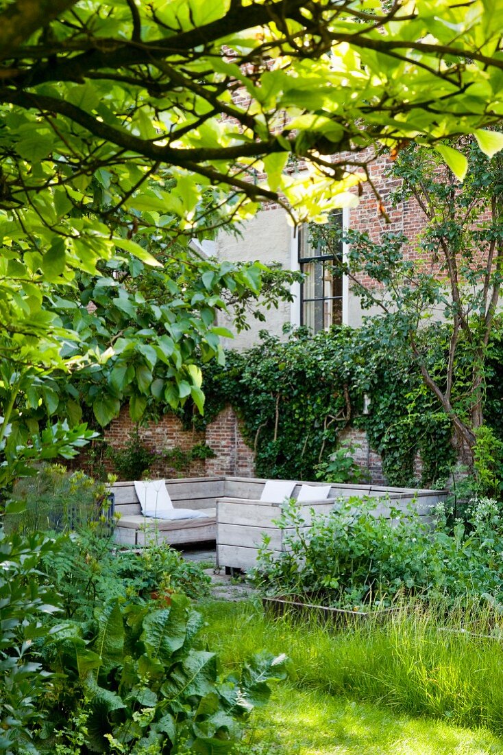 View of seating area against climber-covered brick wall in green garden