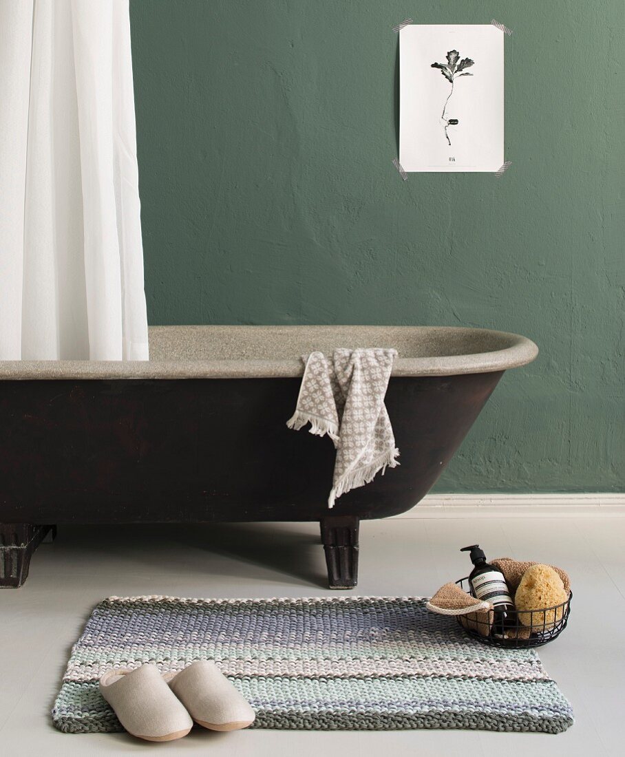 A knitted bath mat in front of a free-standing bath tub
