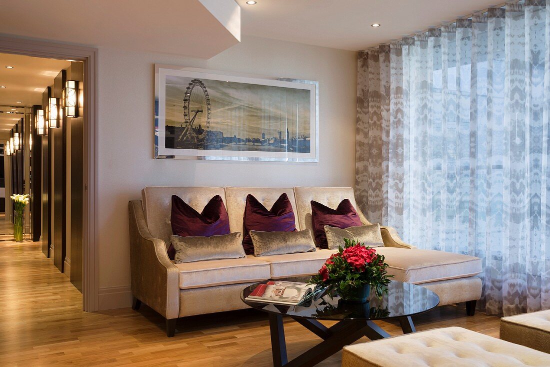 Elegante Sitzecke mit Sofa und rundem Coffeetable vor Fensterfront mit bodenlangen Gardinen