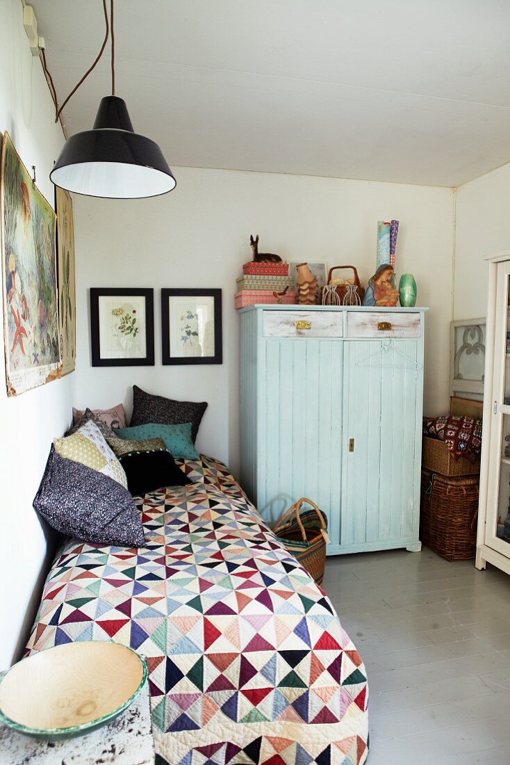 Bunte Quiltdecke auf Einzelbett und verschiedene Kissen in schlichtem Zimmer mit hellblauem Schrank