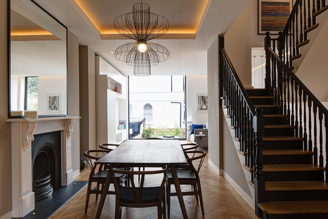 Elegant restaurierte Holztreppe mit schwarz lackiertem Geländer in offenem Wohnraum mit Kamin und modernem Panoramafenster