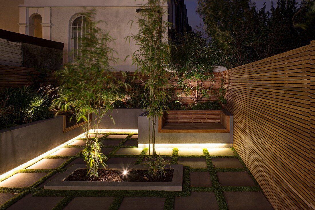 Beleuchteter moderner Reihenhausgarten mit Holz-Sichtschutzwänden und historischem Nachbargebäude