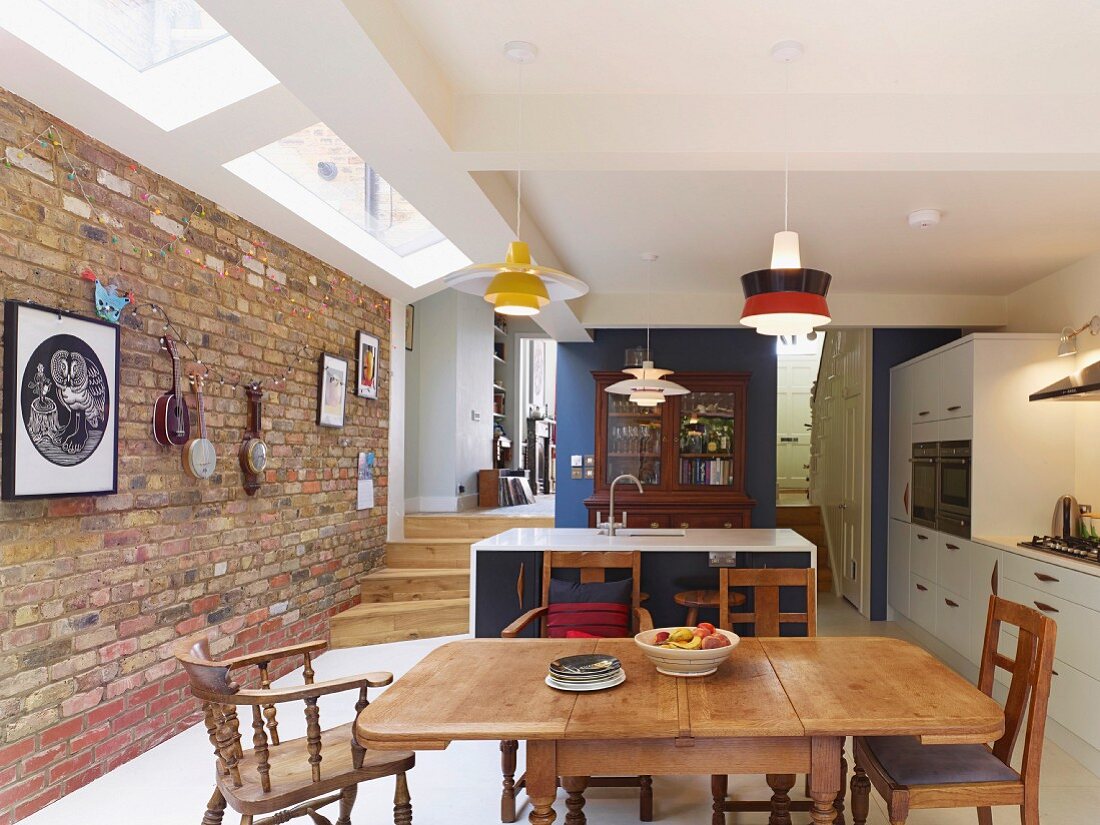 Offene Küche mit traditionellem Essplatz, antikem Vitrinenschrank an blauer Wandscheibe und modernem weißem Oberlichtband an Ziegelwand