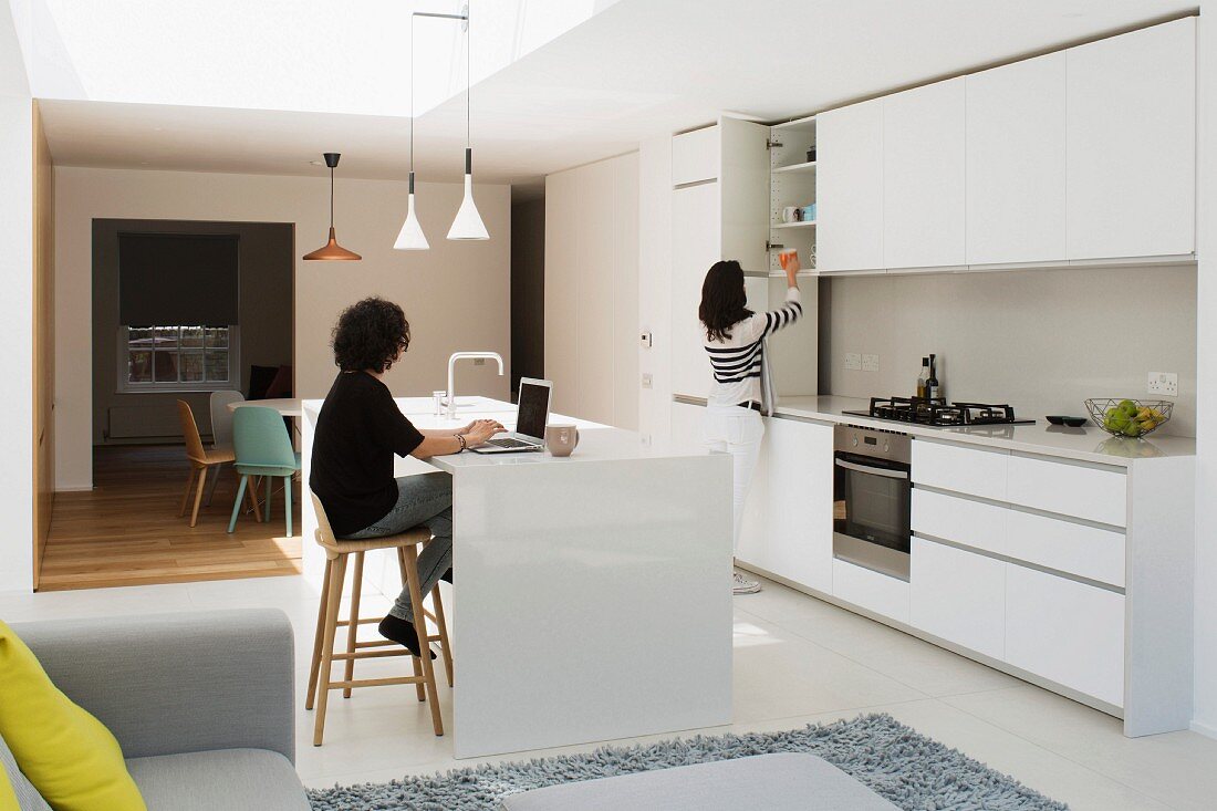 White, open-plan kitchen with island counter, dining area and daylight falling through skylight