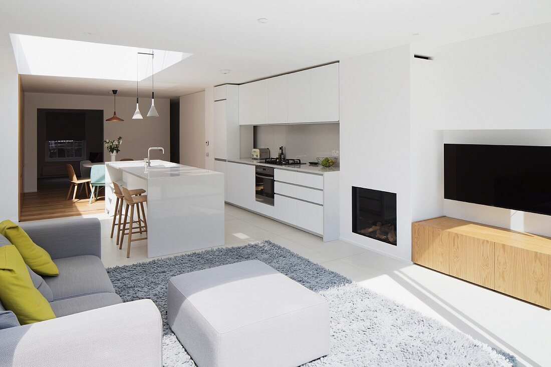 Offenes Wohnen mit weißer Designerküche, Kamin und Plasmabildschirm im Wohnbereich, graue Polstermöbel auf Teppich