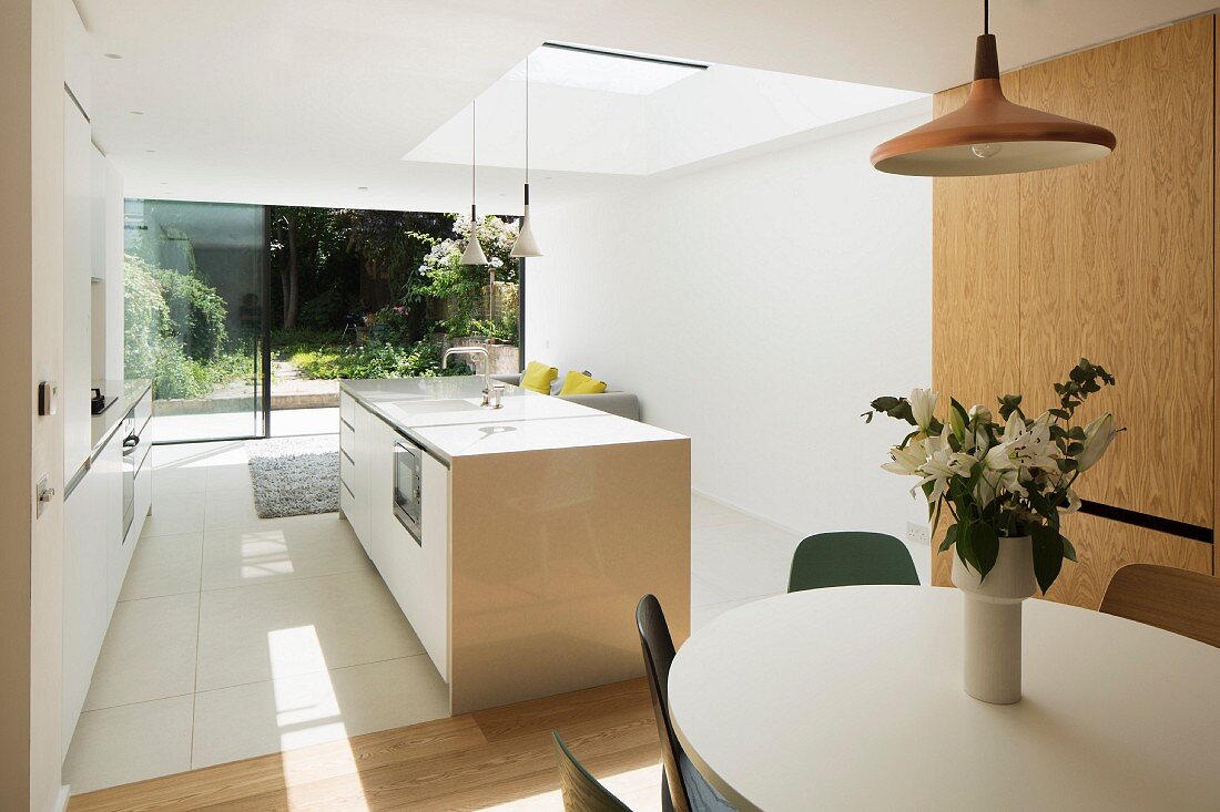 Essplatz mit Blumenstrauß in offener weißer Designerküche, Oberlicht und Blick in den sommerlichen Garten