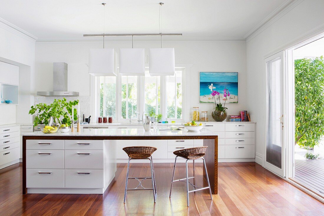 Kitchen island with white base cabinets and bar stools with rattan seat shells in a modern open kitchen