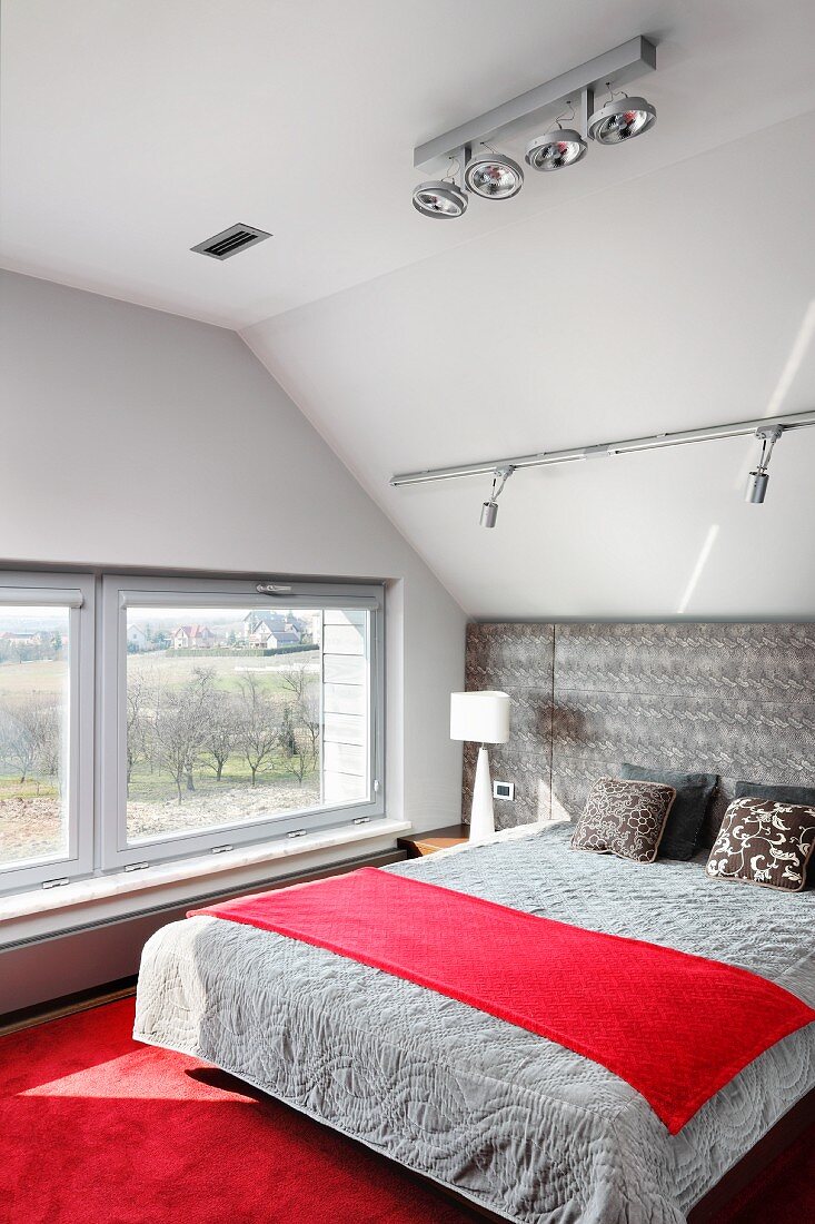 Schlafzimmer mit Dachschräge, rotem Teppichboden und gepolstertem Bettkopfteil