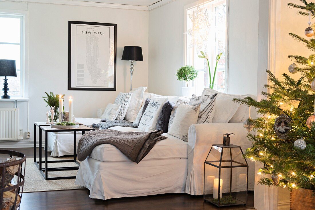 Beleuchteter Weihnachtsbaum vor weißem Sofa mit vielen Kissen