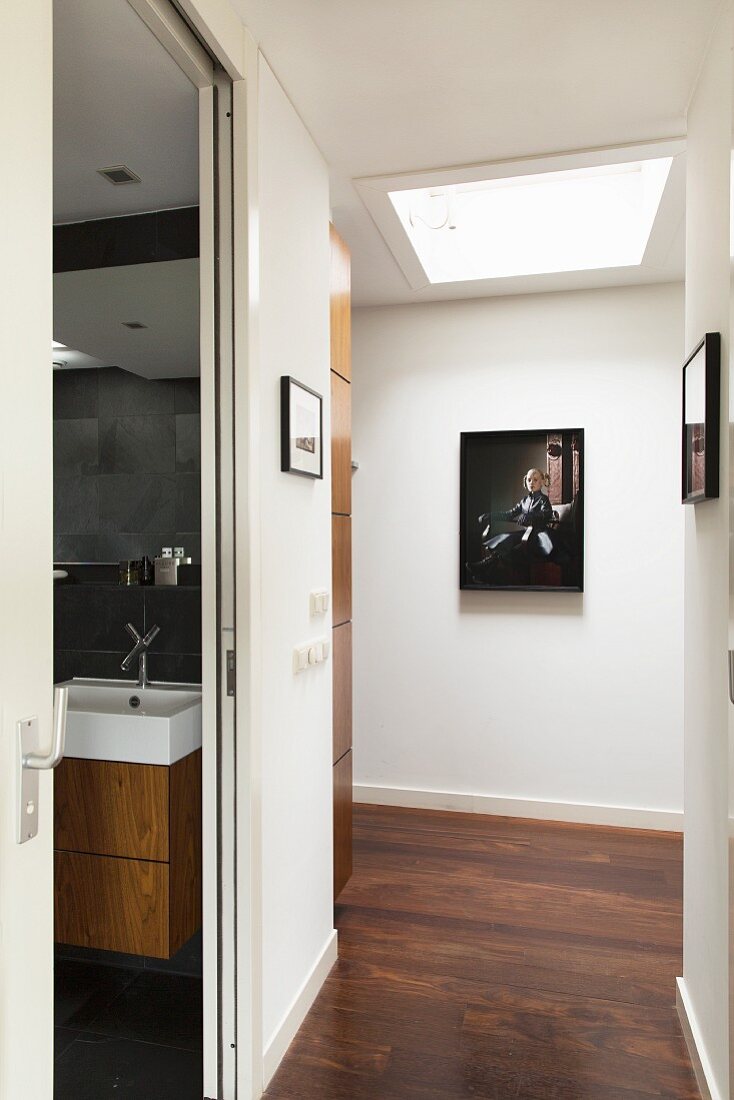 Gangbereich mit Oberlicht in Decke, an Wänden Bilder, seitlich offene Badtür mit Blick auf Waschtisch
