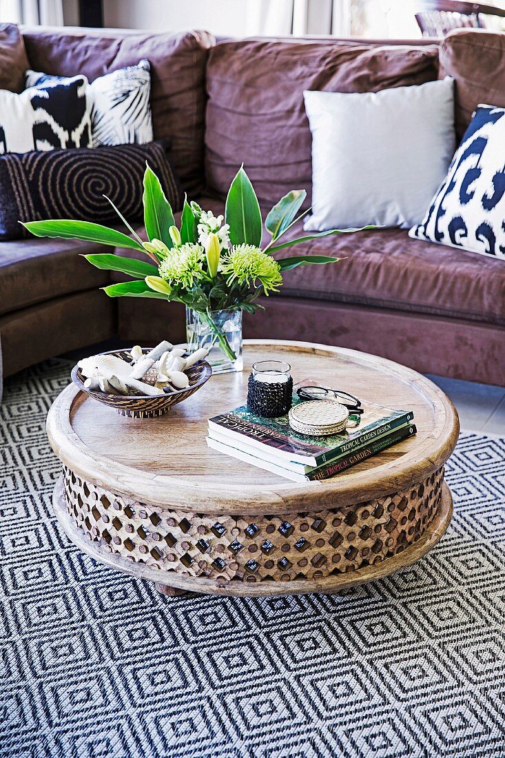 Runder Bodentisch aus verziertem Mangoholz auf geometrisch gemustertem Teppich vor gemütlichem Sofa mit Kissen