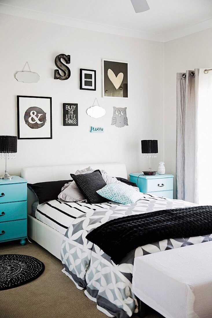 Doppelbett mit schwarz-weißer Bettwäsche, türkisblaue Nachtkästchen und verschiedene Wanddekorationen in Schlafzimmer