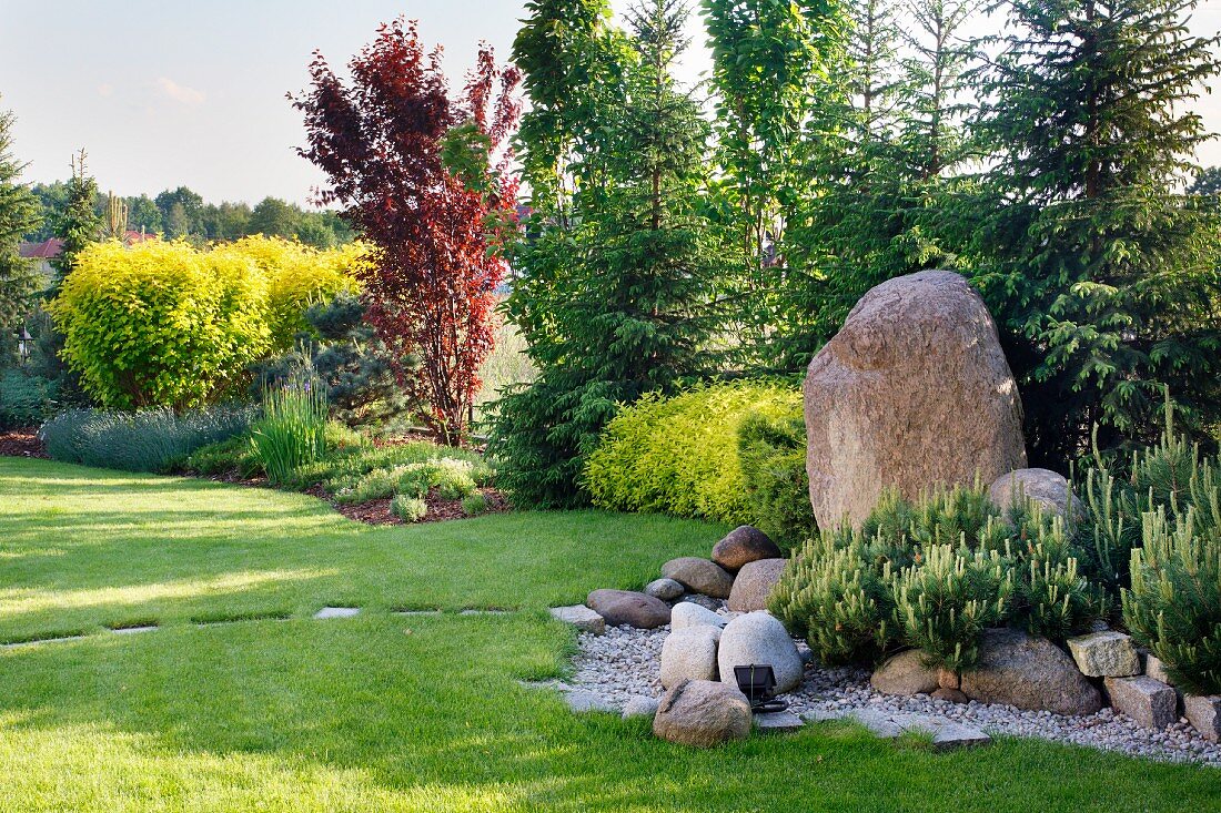Gardens landscaped with boulders and stepping stones in lawn and view of forest