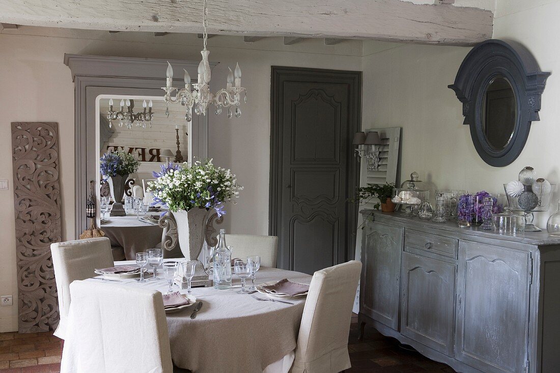 Chairs with pale loose covers around set dining table next to sideboard in rustic dining room